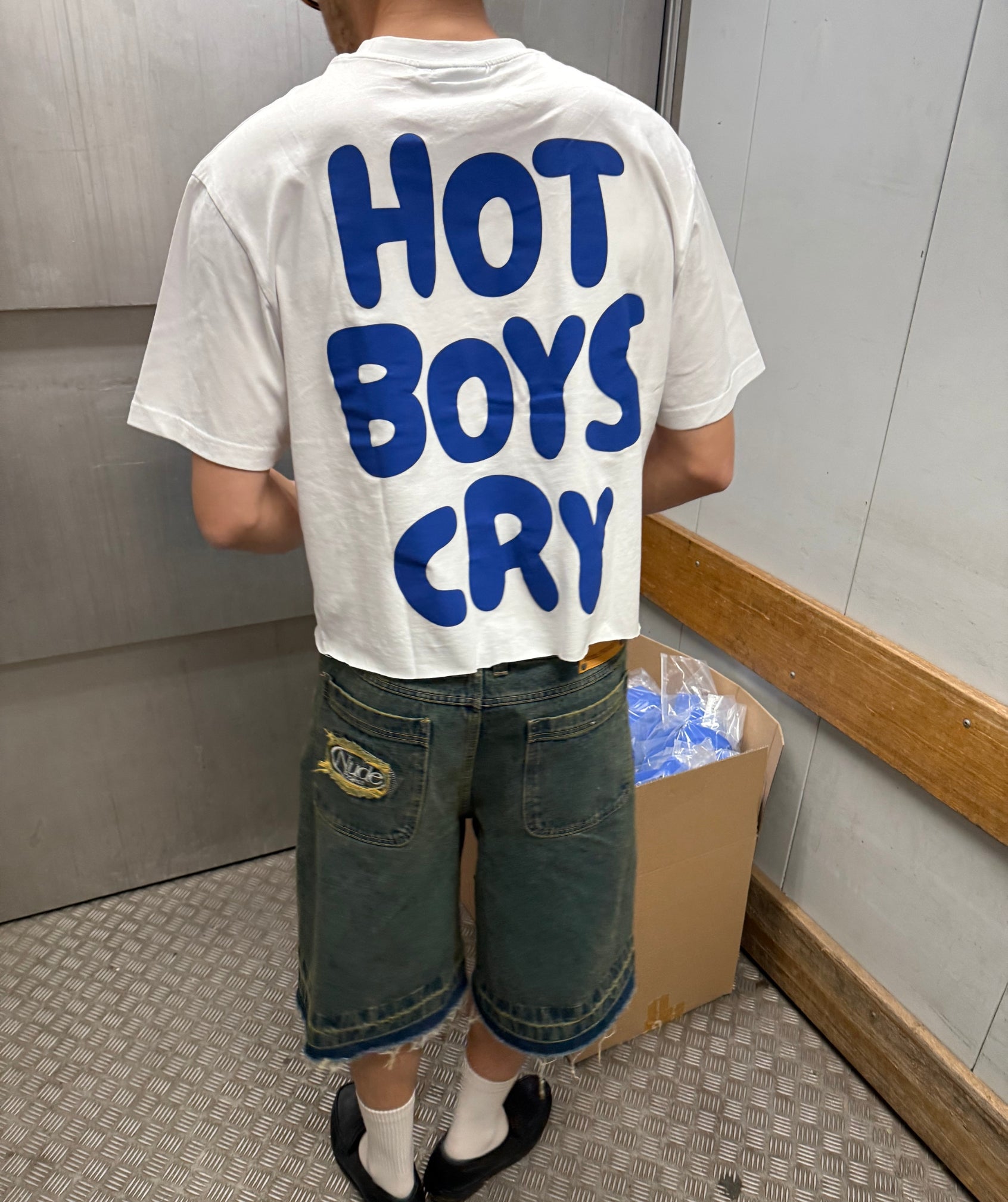 Person wearing a white t-shirt with 'HOT BOYS CRY' in blue text, standing in an indoor setting.