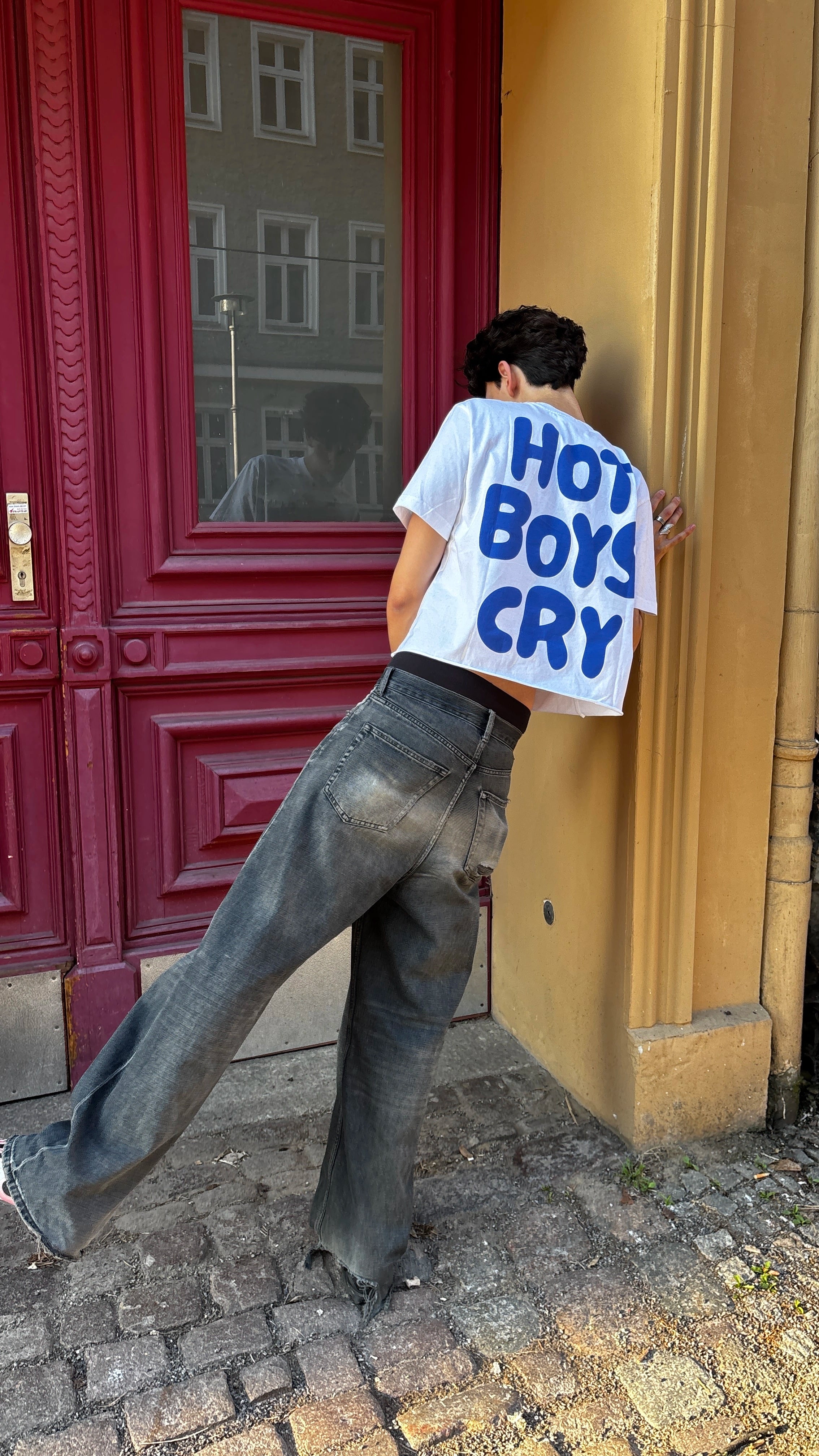 Person wearing a shirt with 'Hot Boys Cry' text against a red door.